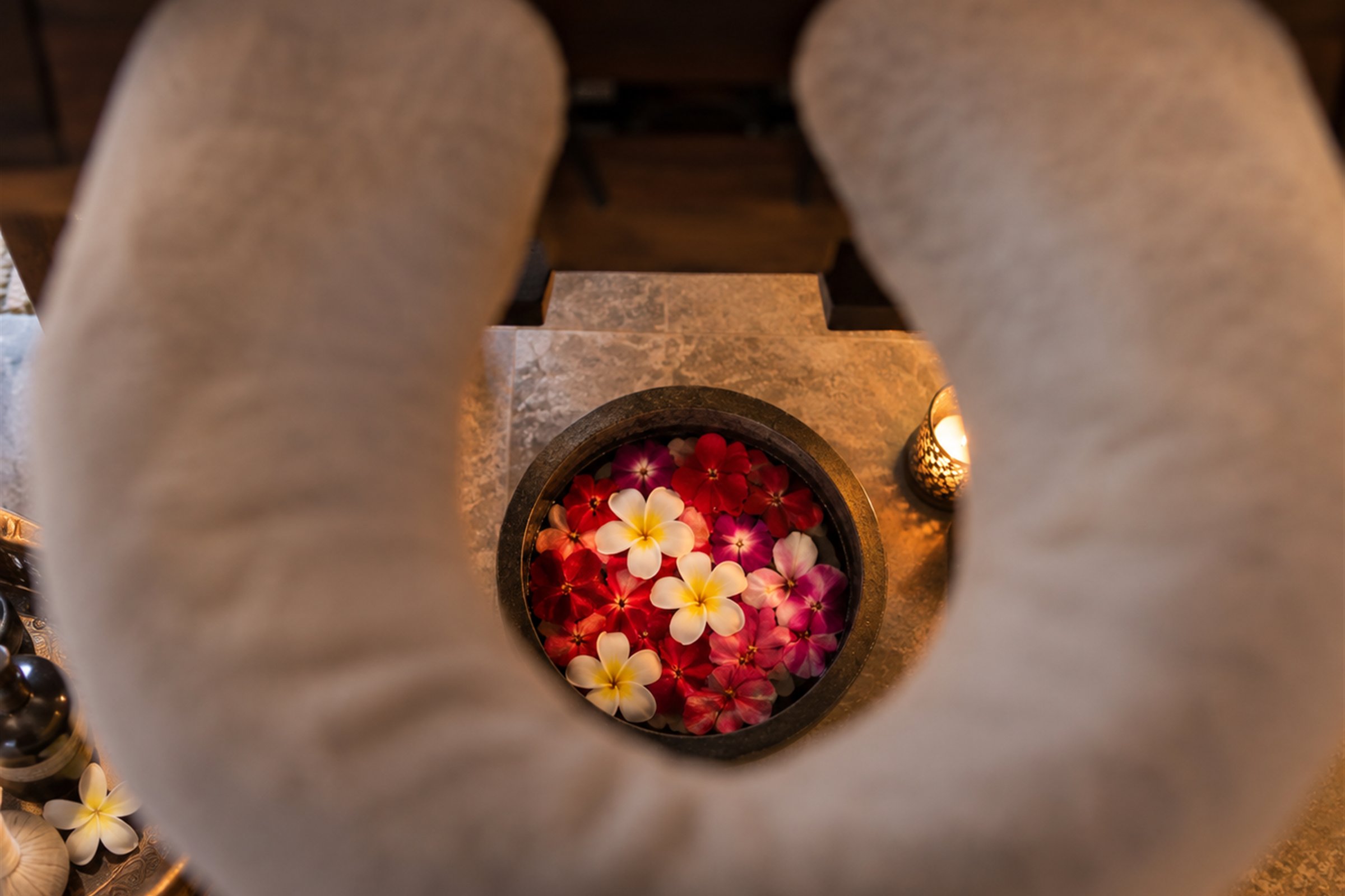 A stone bowl of frangipani and red blossoms set out beside a spa headrest
