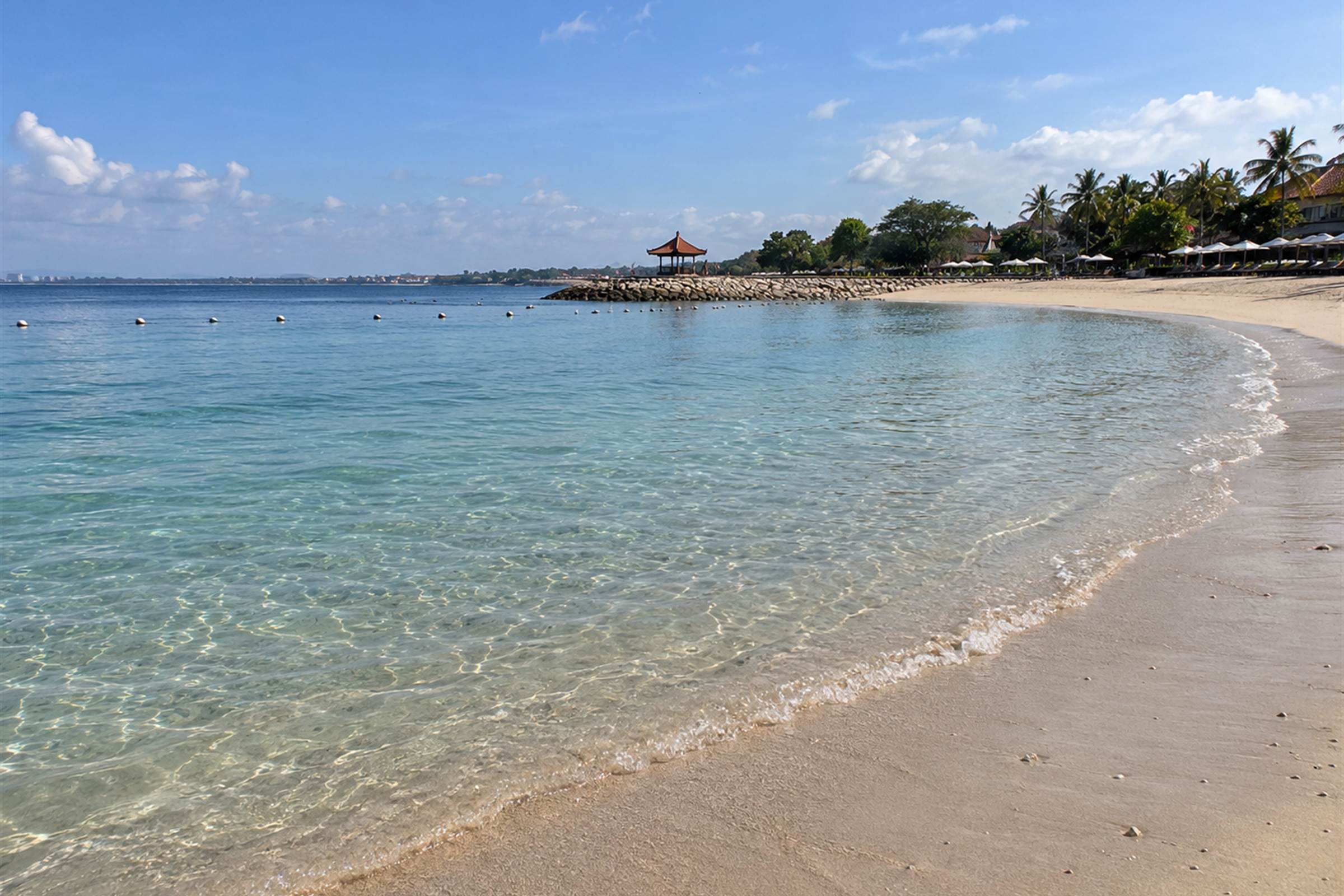 Calm shallow water and pale sand on a sheltered south Bali beach with palms along the shore